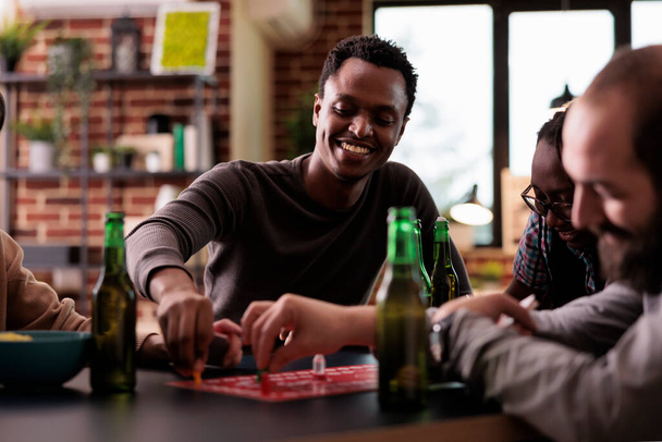 Zelfverzekerde glimlachende Afrikaans-Amerikaanse speler die bordspellen speelt met vrienden thuis. - Foto, afbeelding