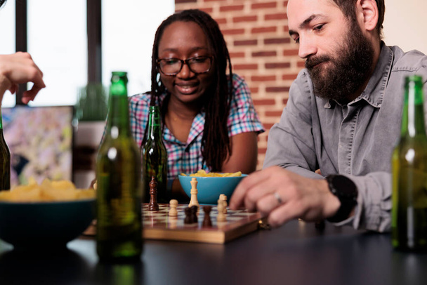 Amigos multiétnicos inteligentes sentados em casa enquanto jogam xadrez juntos. - Foto, Imagem