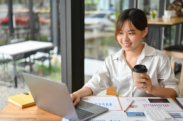 Femme d'affaires professionnelle millénaire asiatique ou analystes financiers travaillant sur le travail de données financières et sirotant café après-midi, assis dans le café. télétravail - Photo, image