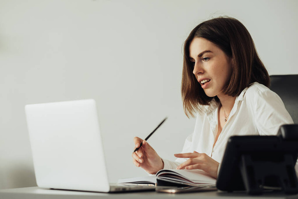 Уверенная молодая женщина, работающая в офисе с ноутбуком, женщина-менеджер записи ноутбука на рабочем месте - Фото, изображение