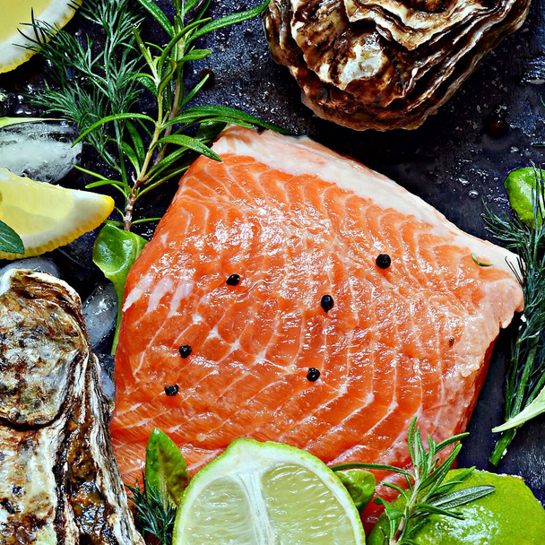 Fresh red salmon (trout) fish steak with fresh oysters, herbs, lemon and lime. Raw fresh seafood flatly, citrus and spices on a dark background. - Фото, изображение