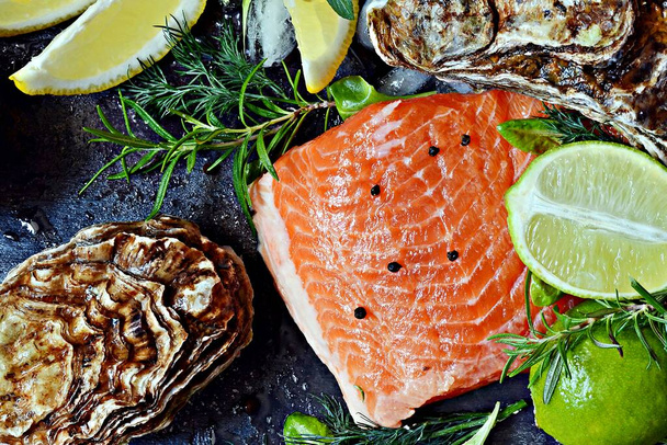 Fresh red salmon (trout) fish steak with fresh oysters, herbs, lemon and lime. Raw fresh seafood flatly, citrus and spices on a dark background. - Zdjęcie, obraz