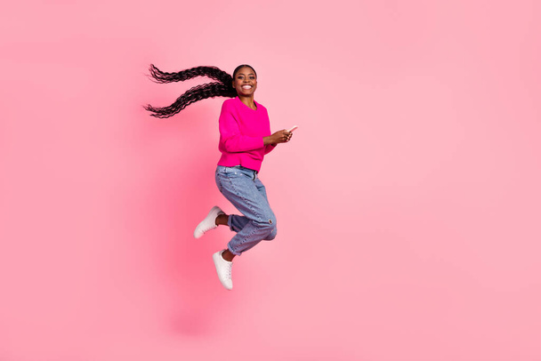 Full size photo of impressed millennial brunette lady hold telephone jump wear pullover jeans shoes isolated on pink background - Φωτογραφία, εικόνα