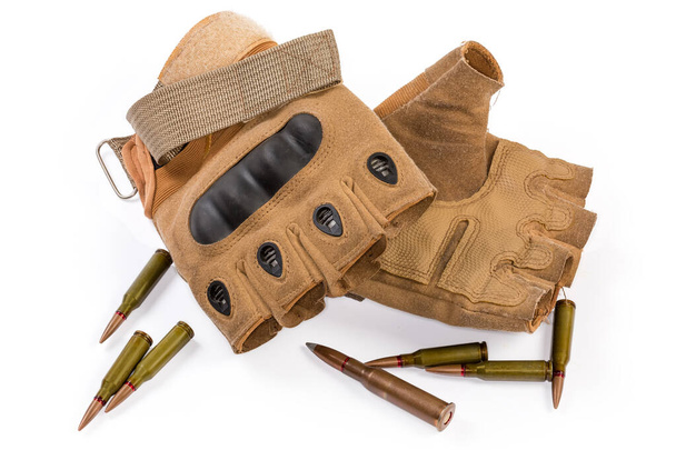 Pair of the used leathern tactical military fingerless gloves with hard knuckle protection among the diferent rifle cartridges on a white background - Fotó, kép