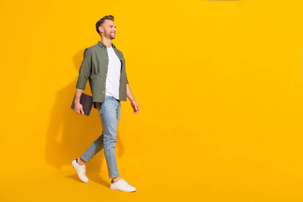 Full length body size view of attractive cheery guy carrying laptop going copy space isolated over vivid yellow color background - Zdjęcie, obraz