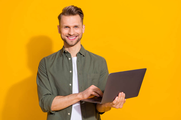 Portrait of attractive cheerful guy using laptop typing email booking order isolated over bright yellow color background - 写真・画像