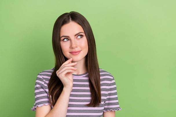 Portrait of attractive pensive cheery brown-haired girl making decision touching chin isolated over bright green color background - Foto, afbeelding