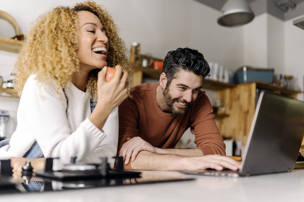 Couple looking at laptop in kitchen. - Foto, Imagen