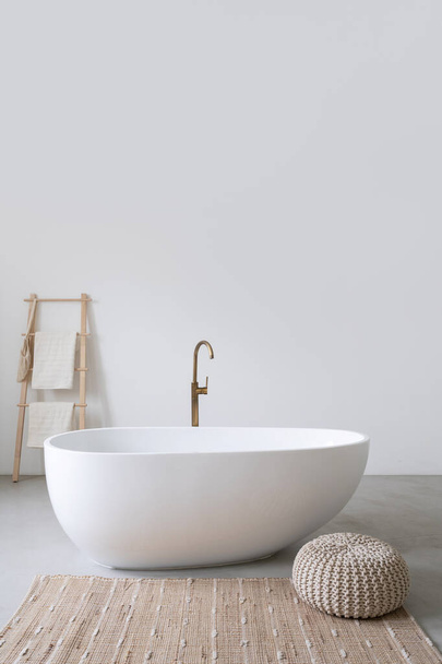 Vertical photo of classic white tub standing with bathroom decor in modern interior against copy space background. Morning routine, spa in hotel resort and contemporary apartment concept - 写真・画像