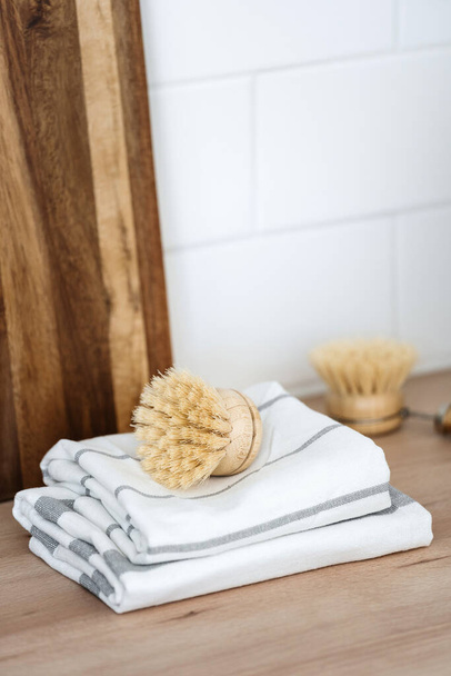 Vertical shot of dishwashing brush with eco friendly material on clean towels against wooden cutting boards at kitchen. Sustainability life. Domestic, housework and home cleaning concepts - Fotó, kép