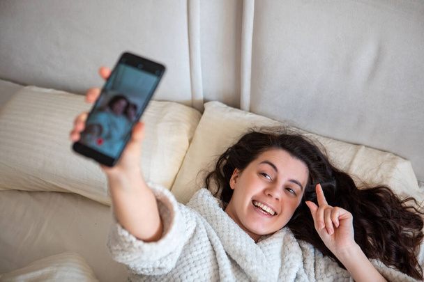 young happy woman taking selfie story laying down in bed - Φωτογραφία, εικόνα