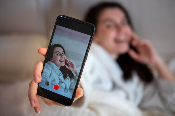 young happy woman taking selfie story laying down in bed - Φωτογραφία, εικόνα