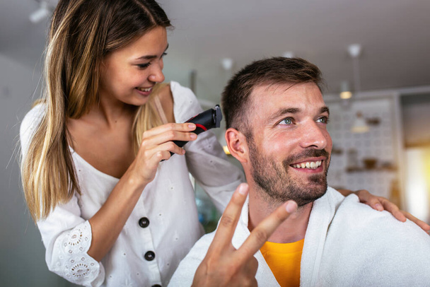 Mujer joven cortando el pelo del hombre usando máquina de afeitar eléctrica en casa.  - Foto, Imagen