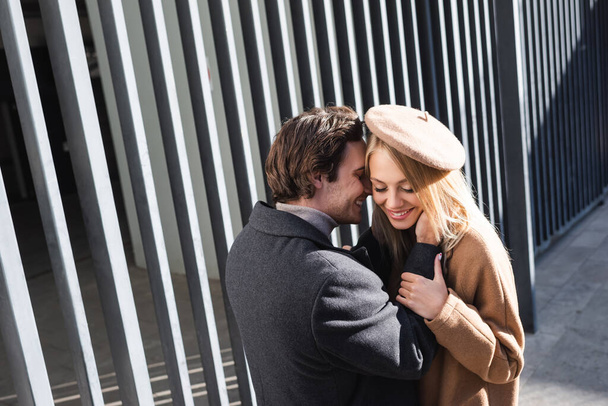 young man embracing cheerful woman in beret near fence outdoors - Foto, immagini