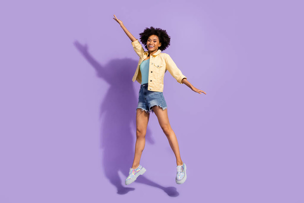 Photo of cute adorable lady wear yellow denim jacket jumping high smiling isolated violet color background - Фото, зображення