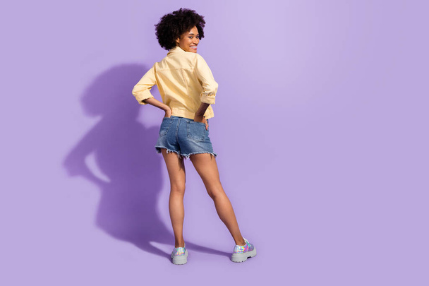 Photo of sweet funny woman dressed yellow jeans jacket standing back dancing isolated purple color background - Φωτογραφία, εικόνα