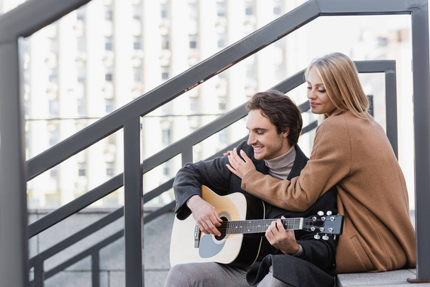 happy woman hugging young man playing acoustic guitar on urban street - Foto, Imagen