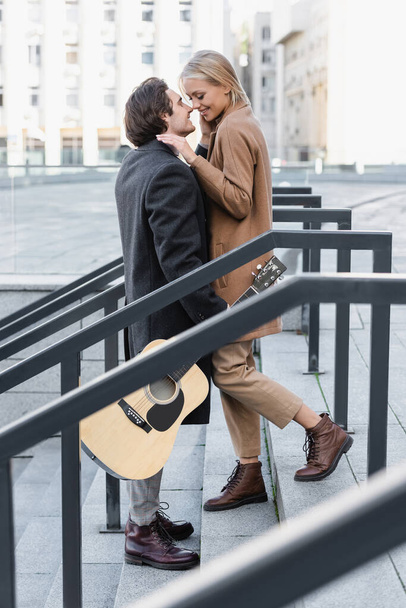 side view of man with acoustic guitar standing on stairs face to face with happy woman - Photo, Image