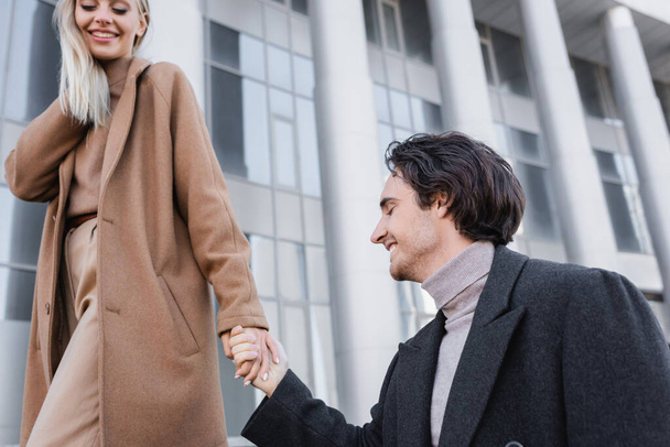 young man holding hands with happy woman in trendy coat outdoors - Foto, Imagem