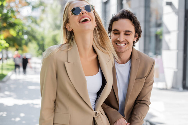 donna bionda in occhiali da sole ridere vicino all'uomo felice sulla strada urbana - Foto, immagini