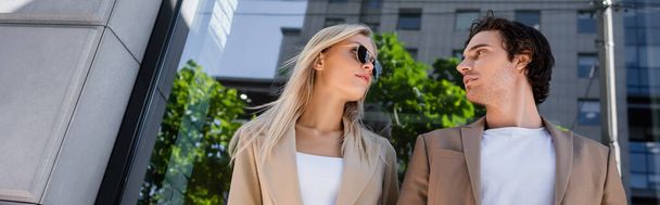 nízký úhel pohledu na mladého muže a blondýnu ve slunečních brýlích, jak se na sebe dívají venku, prapor - Fotografie, Obrázek
