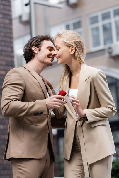 sonriente hombre haciendo matrimonio propuesta a elegante mujer rubia en la calle urbana - Foto, Imagen