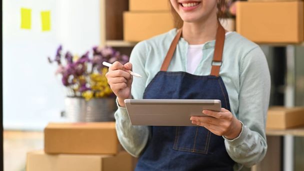 Young female startup business owner working with digital tablet for checking order on internet - 写真・画像