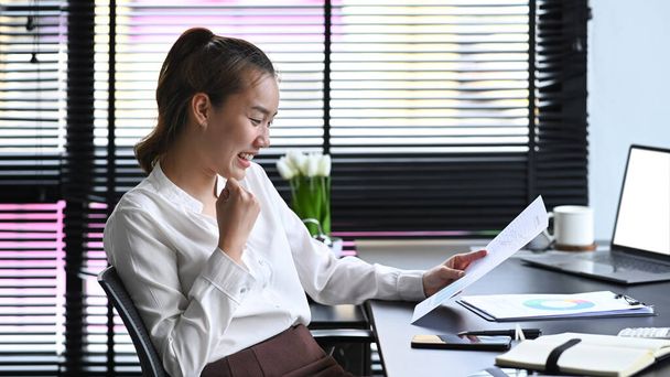 Happy young female employee reading good news on digital tablet and celebrating success. - 写真・画像