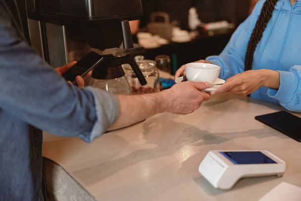 Женщина вручает чашку кофе или чая клиенту-мужчине за стойкой. Barista обслуживает клиентов в баре. - Фото, изображение