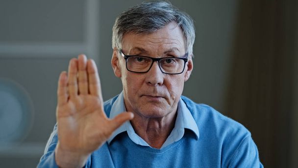 Serious old senior mature 60s man stretch out palm to camera says stop gesture indoors. Social problems older generation disrespect ban refusal disagreement. Aged businessman trouble denial rejection - Foto, Bild