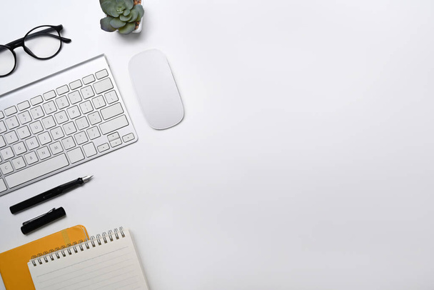 Белый рабочий стол с беспроводной клавиатурой, очками, ноутбуком и сочным растением - Фото, изображение