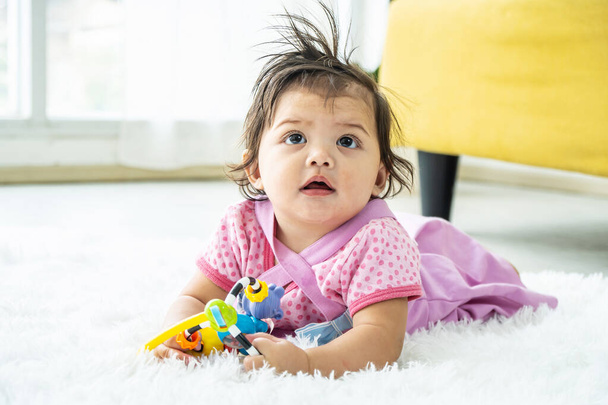 Милая девочка ложится и играет в игрушки на мягком коврике в спальне. Игрушки для маленьких детей. Интерьер для детской для мальчиков. Ребенок с развивающей игрушкой. Раннее развитие. - Фото, изображение