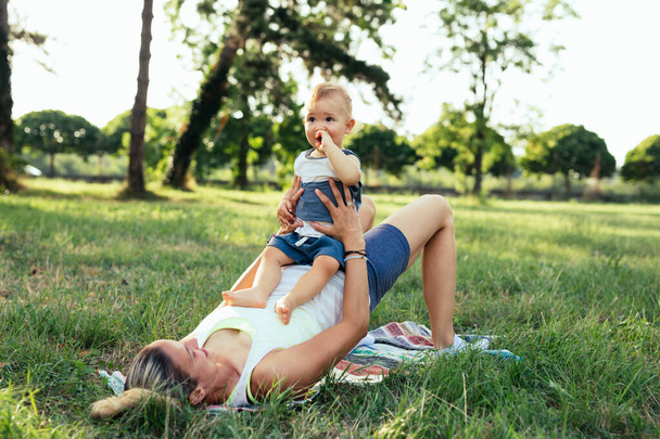 young caucasian mother and her son exercises outdoor in public park - Photo, Image