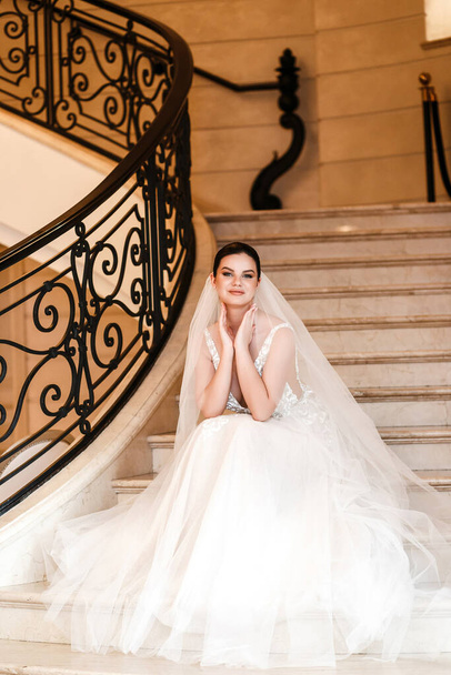 A stylish bride sits on the steps of a marble staircase. - Photo, Image
