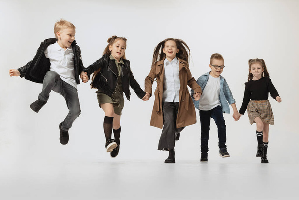 Happy school and preschool age children, girls and boys running, jumping isolated on grey studio background. Beauty, kids fashion, education, happy childhood concept. - Fotoğraf, Görsel