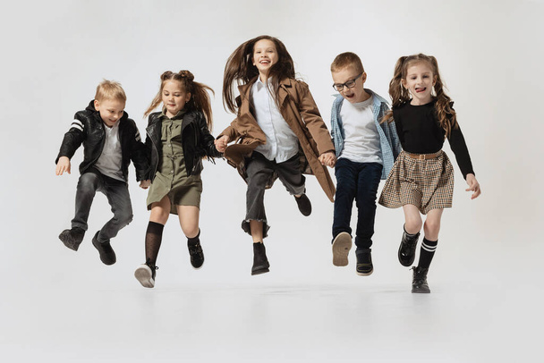 Emotional school and preschool age children, girls and boys running, jumping isolated on grey studio background. Beauty, kids fashion, education, happy childhood concept. - Foto, immagini