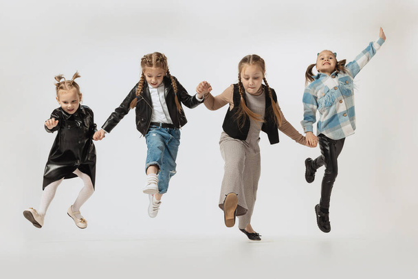 Happy school and preschool age children, beautiful girls jumping isolated on grey studio background. Beauty, kids fashion, education, happy childhood concept. - Zdjęcie, obraz