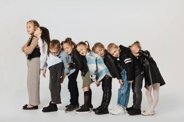 Group of happy cute kids, little girls and boys in modern outfits standing isolated on grey studio background. Beauty, kids fashion, education, happy childhood concept. - Photo, image