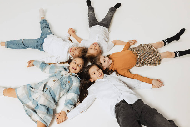 Aerial view of happy smiling school kids lying in circle and looking at camera. Beauty, kids fashion, education, happy childhood concept. - Fotografie, Obrázek