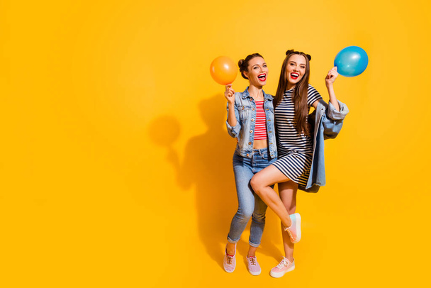 Full body portrait of charming cheerful girls have fun hold air balloons isolated on yellow color background - 写真・画像