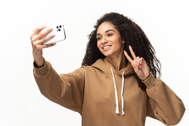 Happy carefree African-American young woman with curly hair taking selfie on the smartphone, recording video message, streaming in social medias - Φωτογραφία, εικόνα