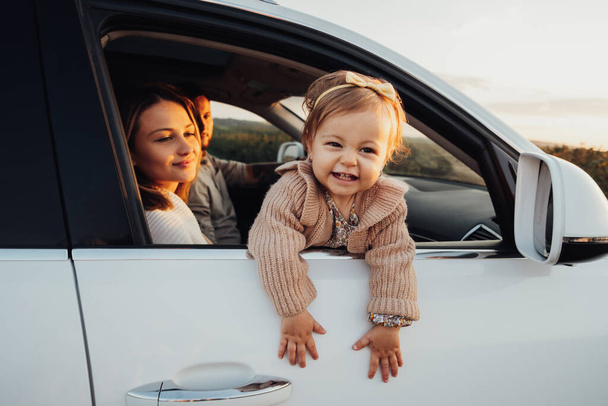 κοριτσάκι κοιτάζοντας έξω από το παράθυρο του αυτοκινήτου, νεαρή οικογένεια με την κόρη του μωρού σε ένα οδικό ταξίδι στο ηλιοβασίλεμα - Φωτογραφία, εικόνα