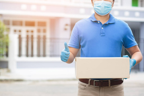 小包配達人は保護手袋青とマスクを着用し、自宅へのサービスを通じてパッケージの衛生生殖器と細菌を保護します。手押しの契約と箱を受け取る顧客の提出 - 写真・画像
