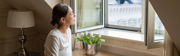 dreamy woman looking away through window near fresh tulips, banner - Foto, Imagem