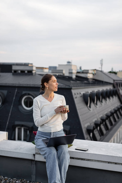 woman with clay cup sitting on rooftop near laptop and mobile phone - Photo, image