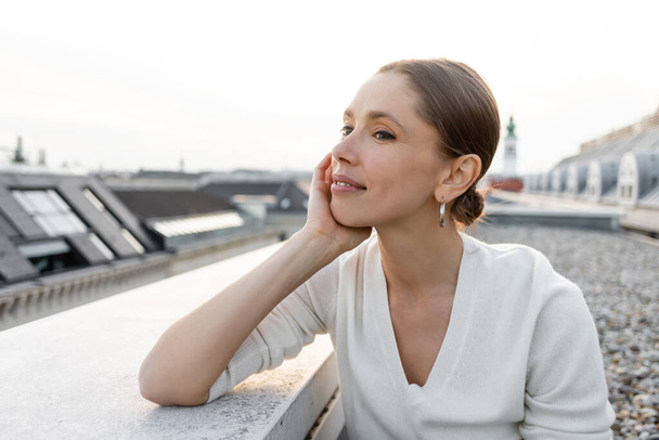 thoughtful woman smiling while looking away on rooftop - Photo, image