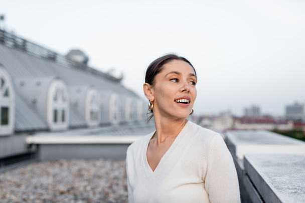 happy woman in white jumper looking away on rooftop - Foto, Imagen