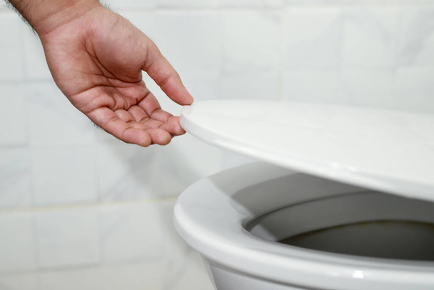 рука людини відкриває кришку туалету
 - Фото, зображення
