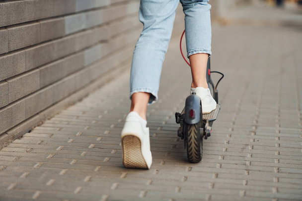 Close up view of girl in casual clothes that riding electric schooter outdoors at sunny daytime. - Фото, зображення