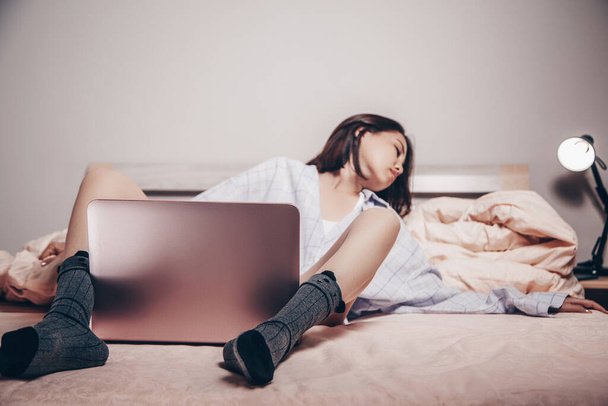 mladý asijský webkamera modelka dívka leží před notebookem s nohama roztaženýma. si užívá a ukazuje svůj šarm. nízká hloubka zaměření, selektivní zaměření. - Fotografie, Obrázek